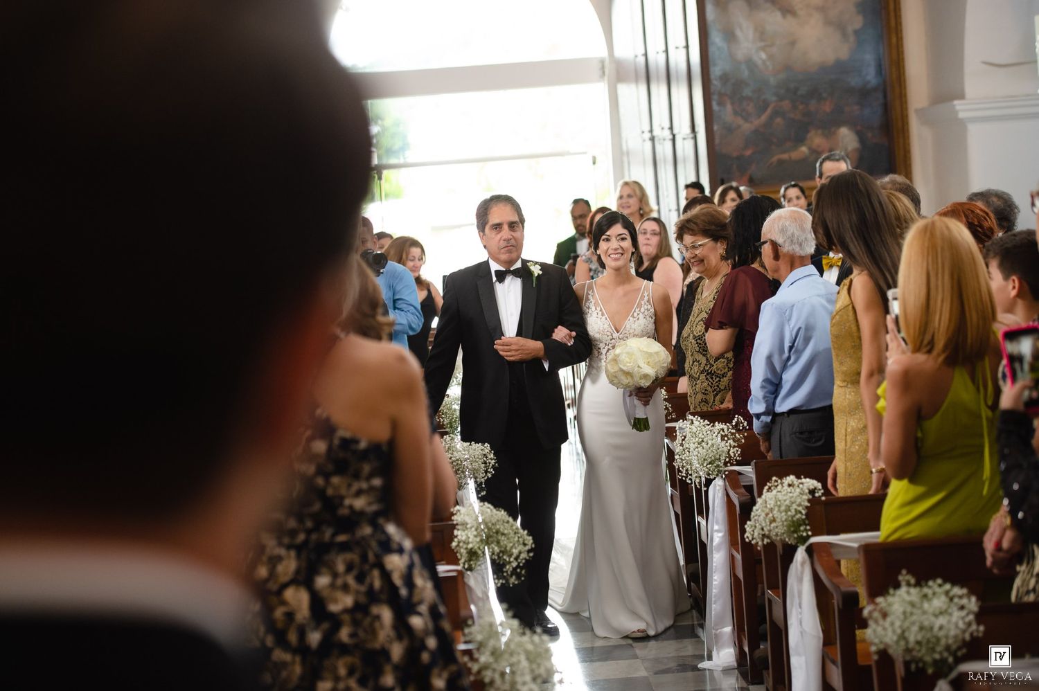 Bride walks down church aisle with escort at elegant wedding ceremony, guests seated in pews.