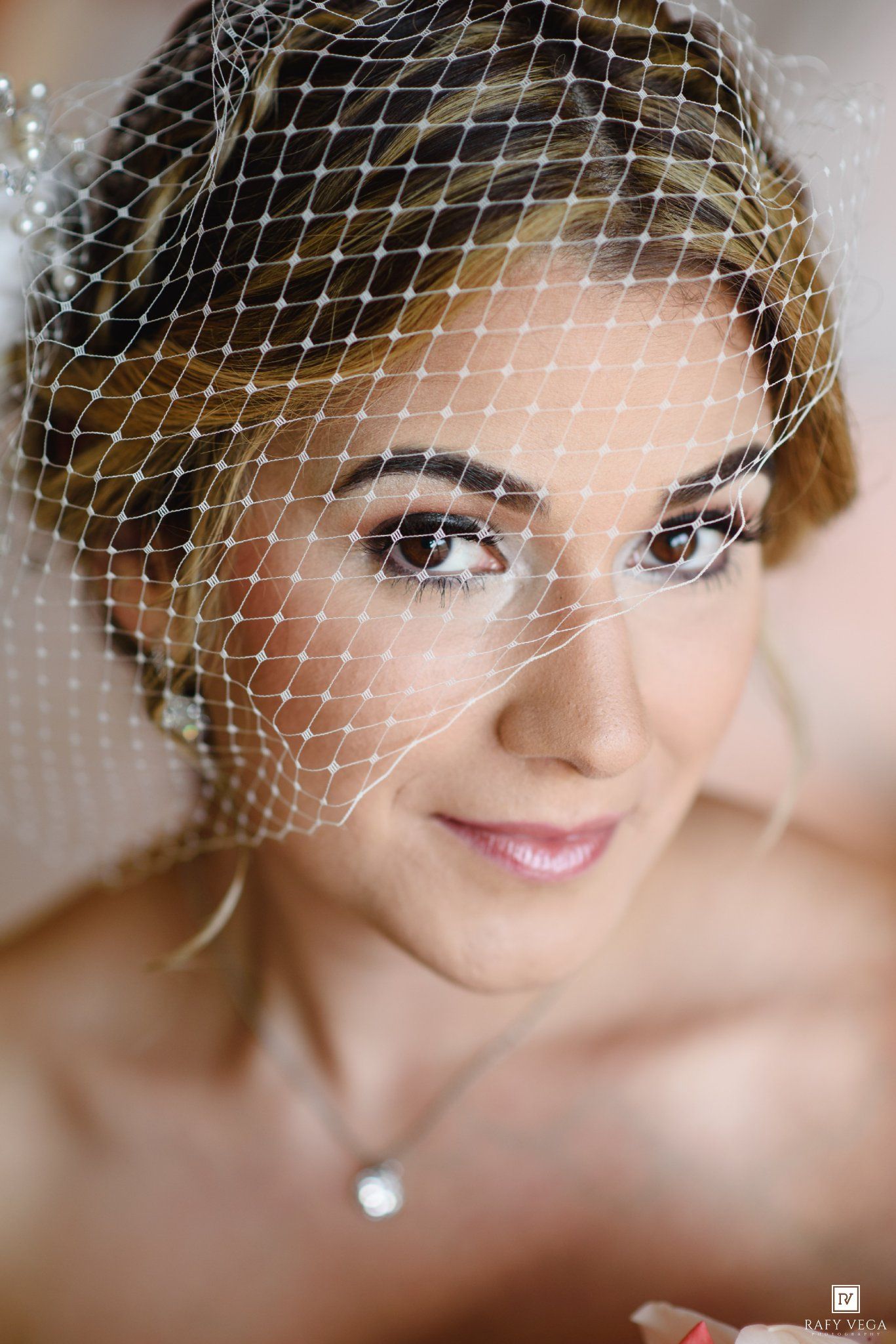 Close-up portrait of a bride wearing a birdcage veil and pearl necklace with elegant bridal makeup.