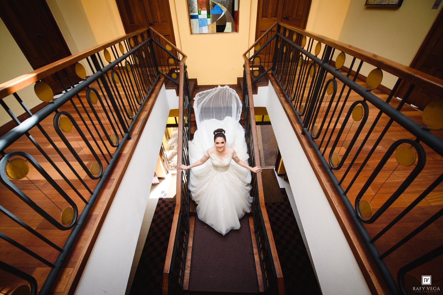 Bride in white gown and veil descends grand staircase with bridesmaids at elegant wedding venue.