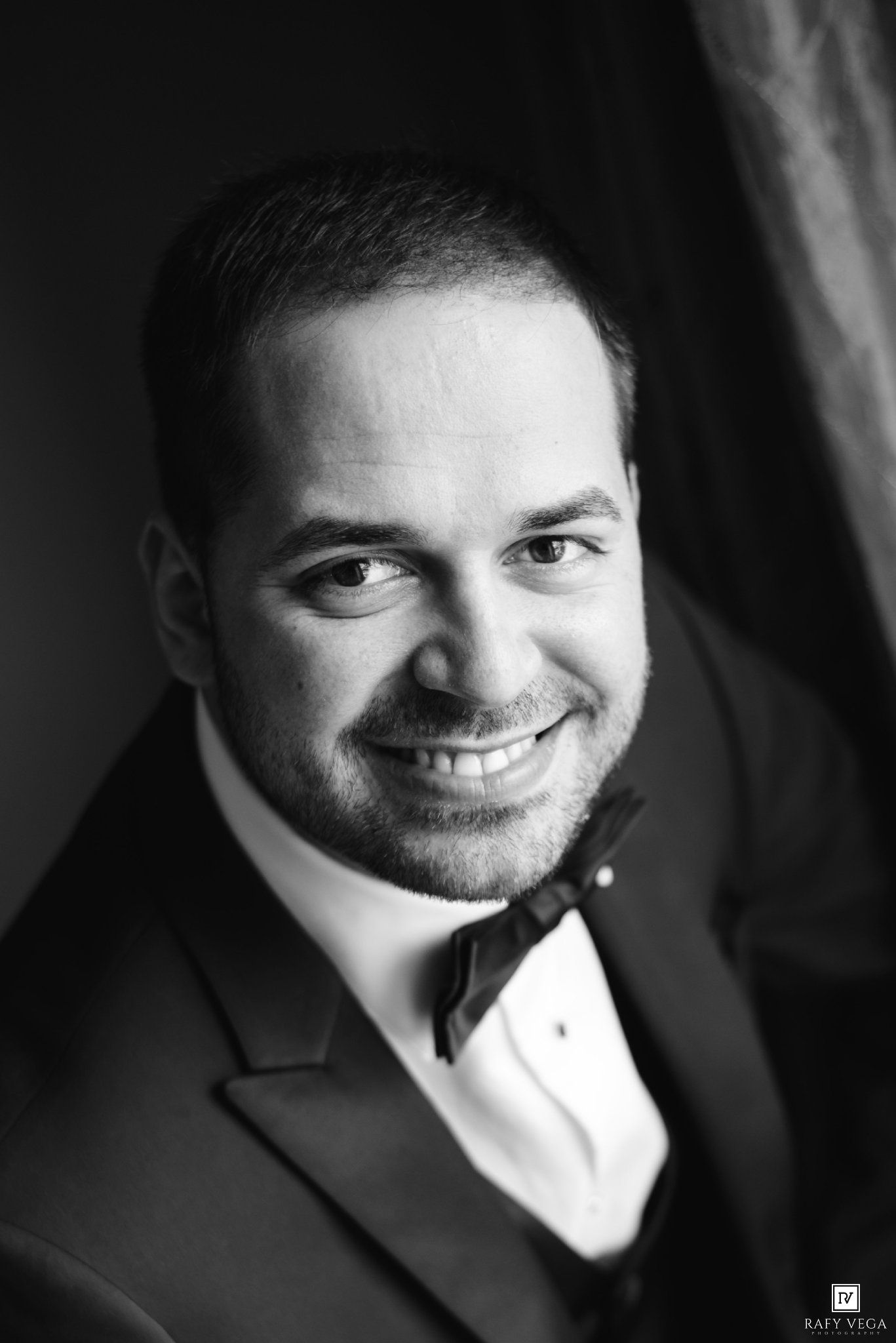 Black and white portrait of a smiling man in a tuxedo with bow tie, elegant formal attire photography.
