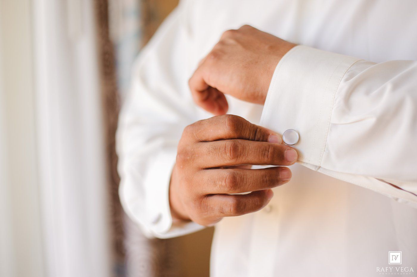 Groom fastening silver cufflinks on white dress shirt sleeves while preparing for wedding ceremony.
