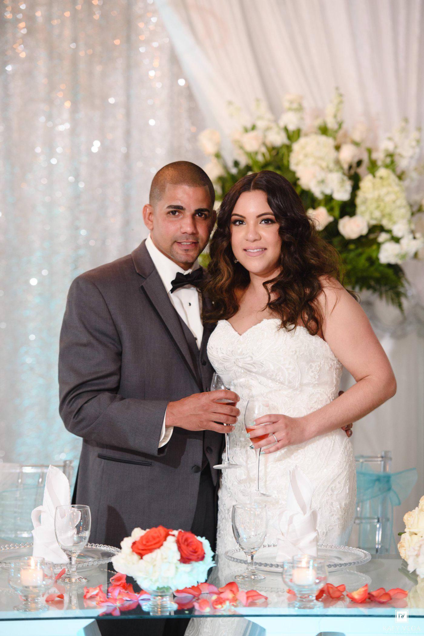 Bride and groom posing together at wedding reception table with floral arrangements and champagne glasses.