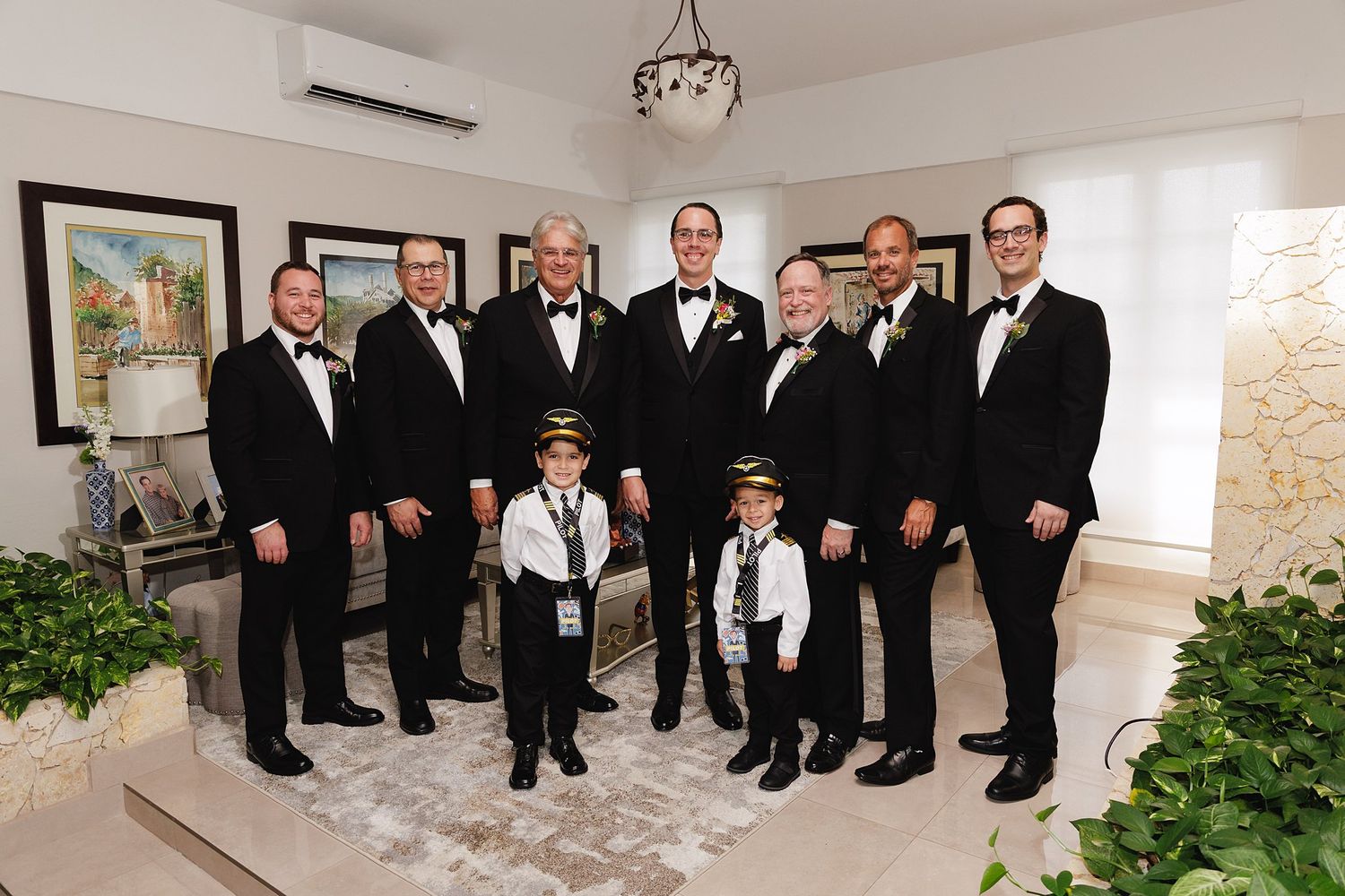 Group of men in tuxedos with two young boys in pilot costumes posing together at a formal wedding celebration.