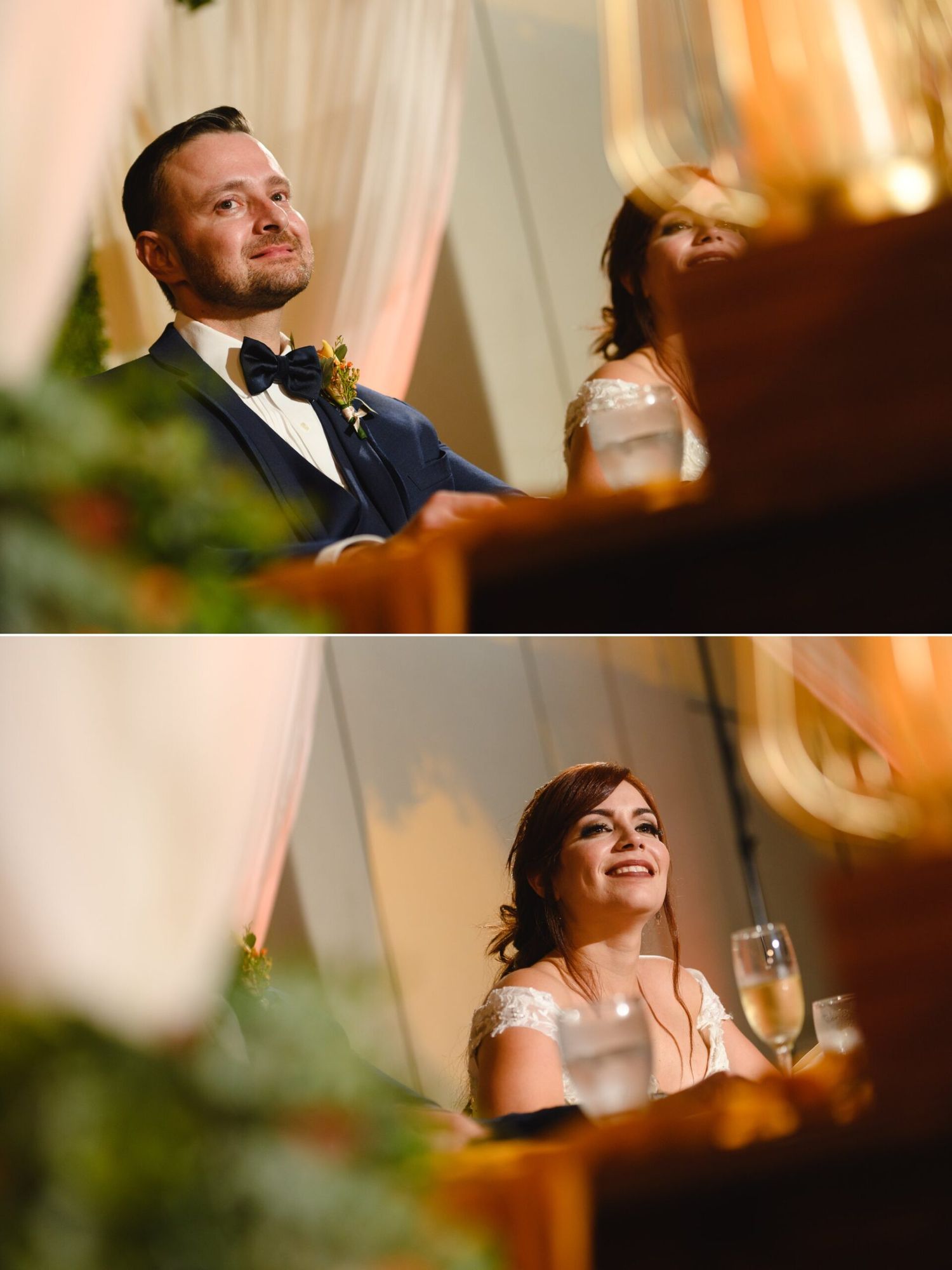 A groom in a navy suit smiles emotionally during wedding speeches, while his bride laughs joyfully holding a champagne glass.
