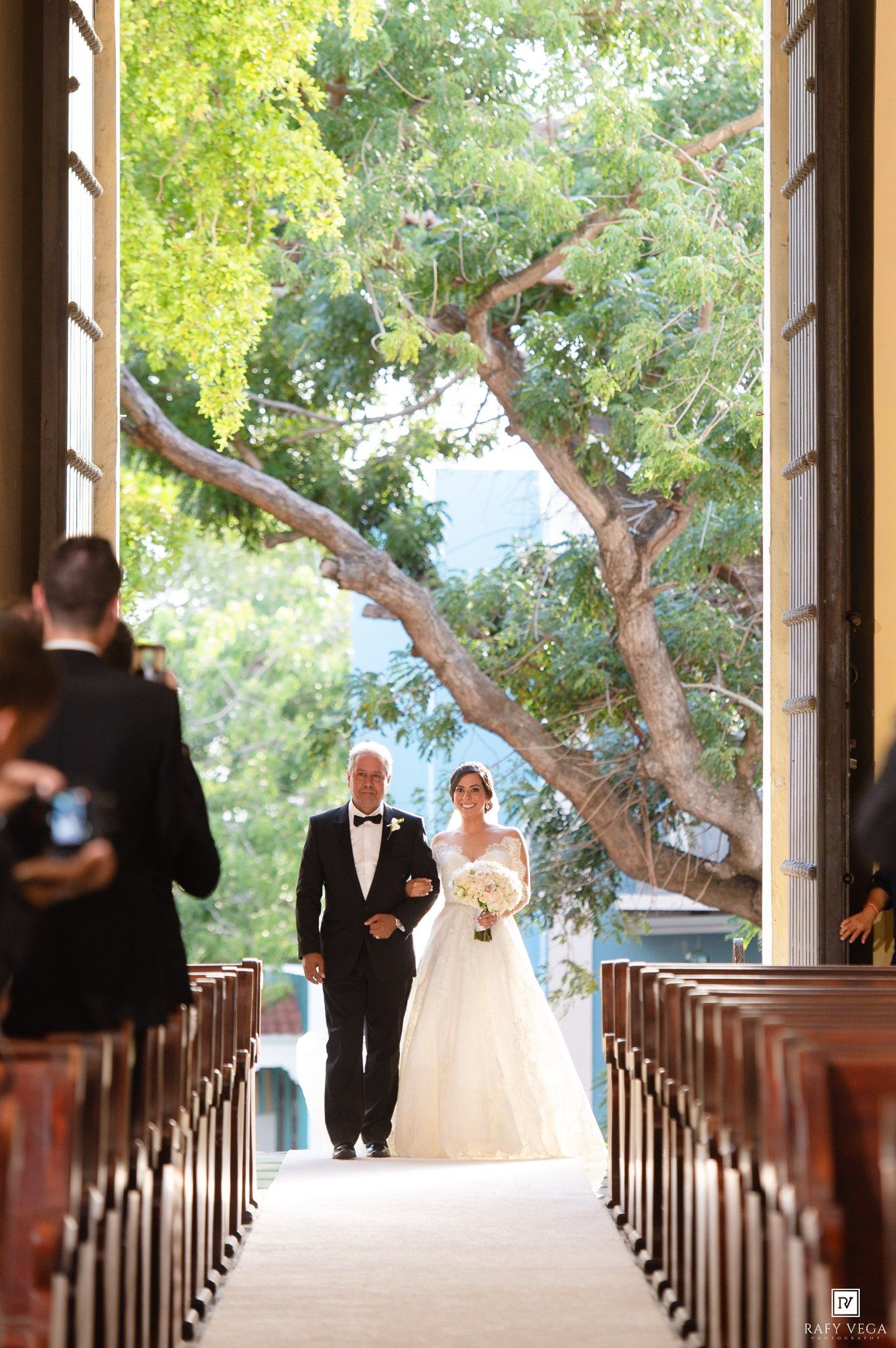 Bride walking down the aisle with her father in a sunlit church chapel during a wedding ceremony.