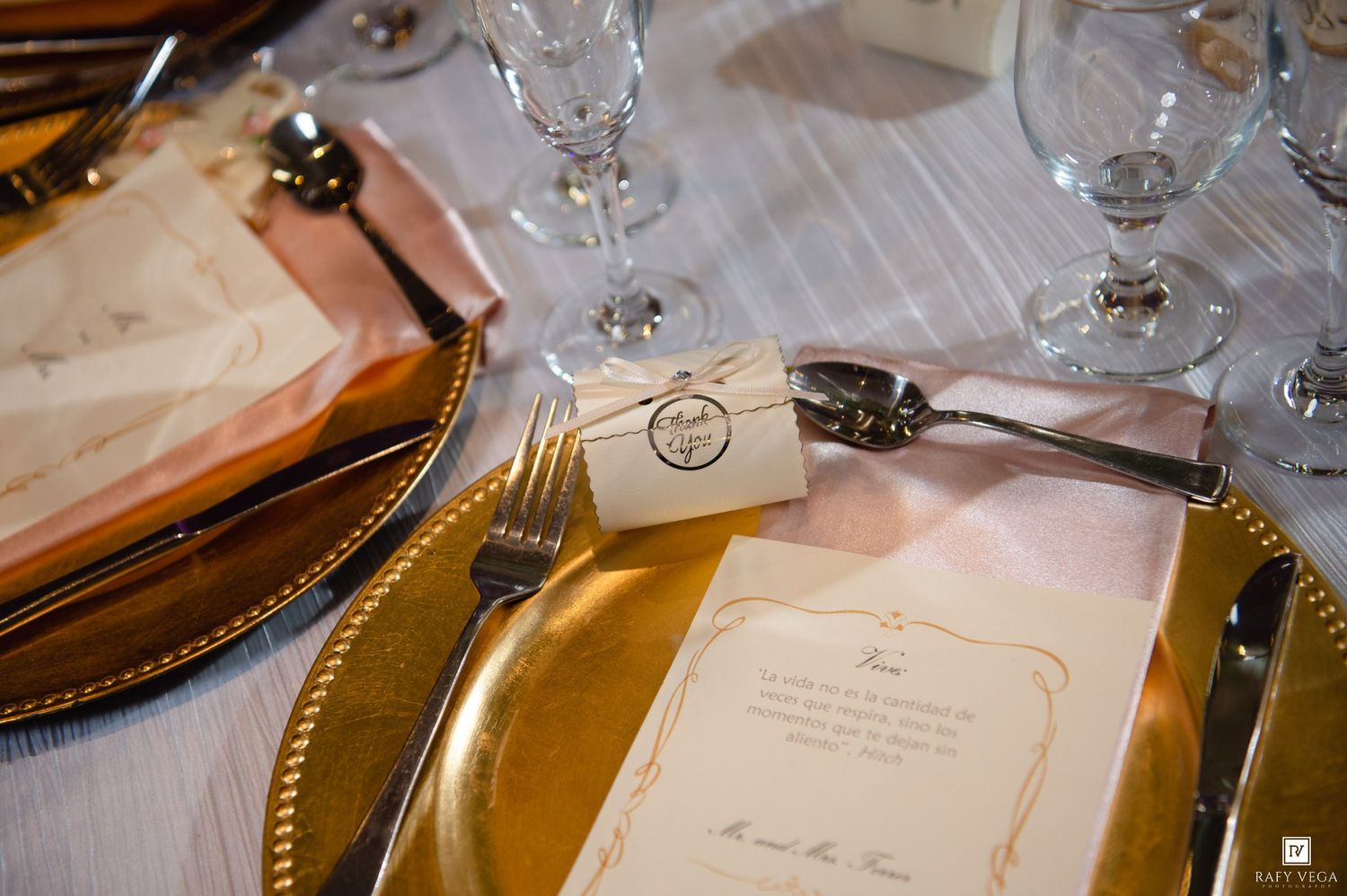 Elegant wedding table setting with gold charger plates, crystal glasses, and personalized menu cards with gift tags.