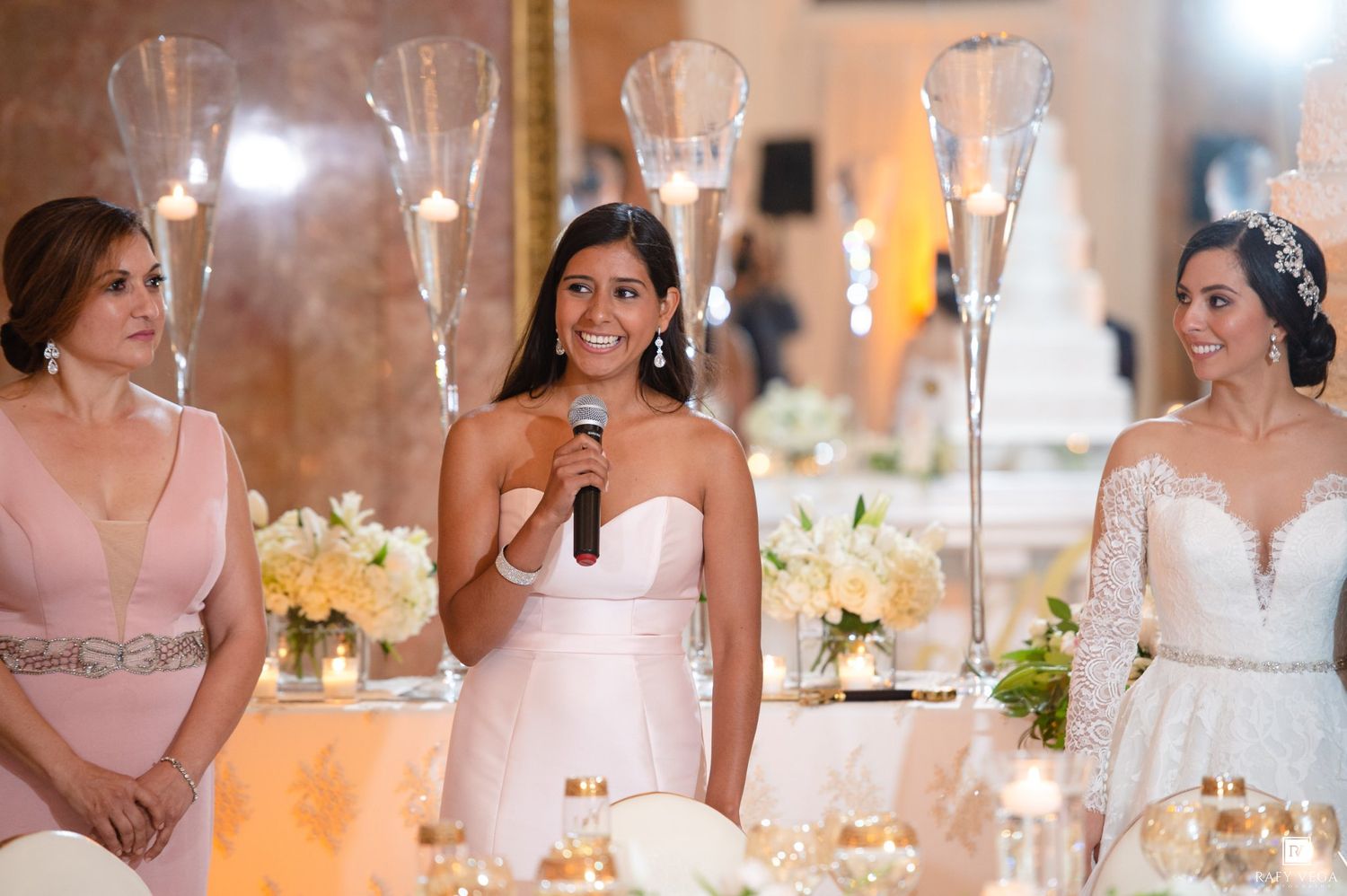 Bridesmaid gives a heartfelt speech at elegant wedding reception with bride in lace gown and floral centerpieces.
