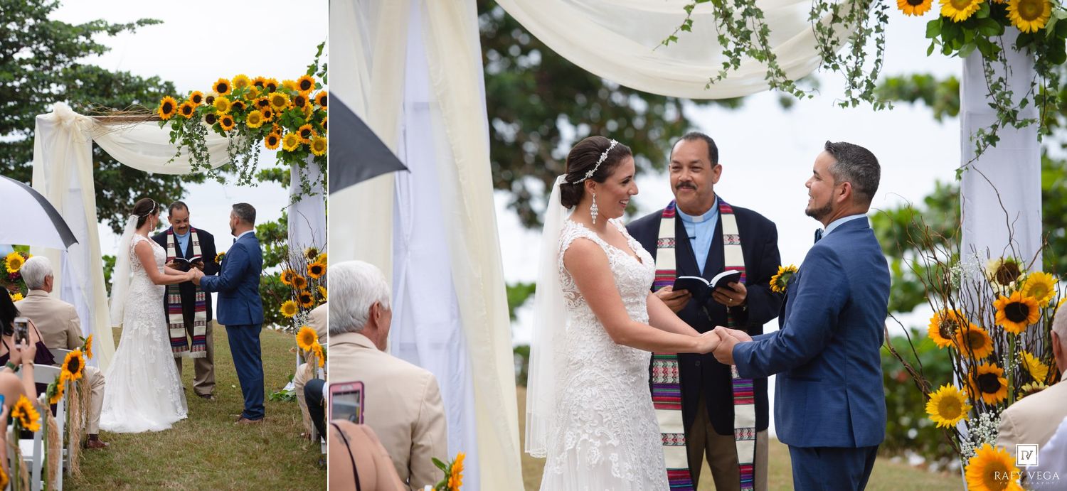 A couple exchanges vows at an outdoor wedding ceremony decorated with sunflowers under a white draped arch.