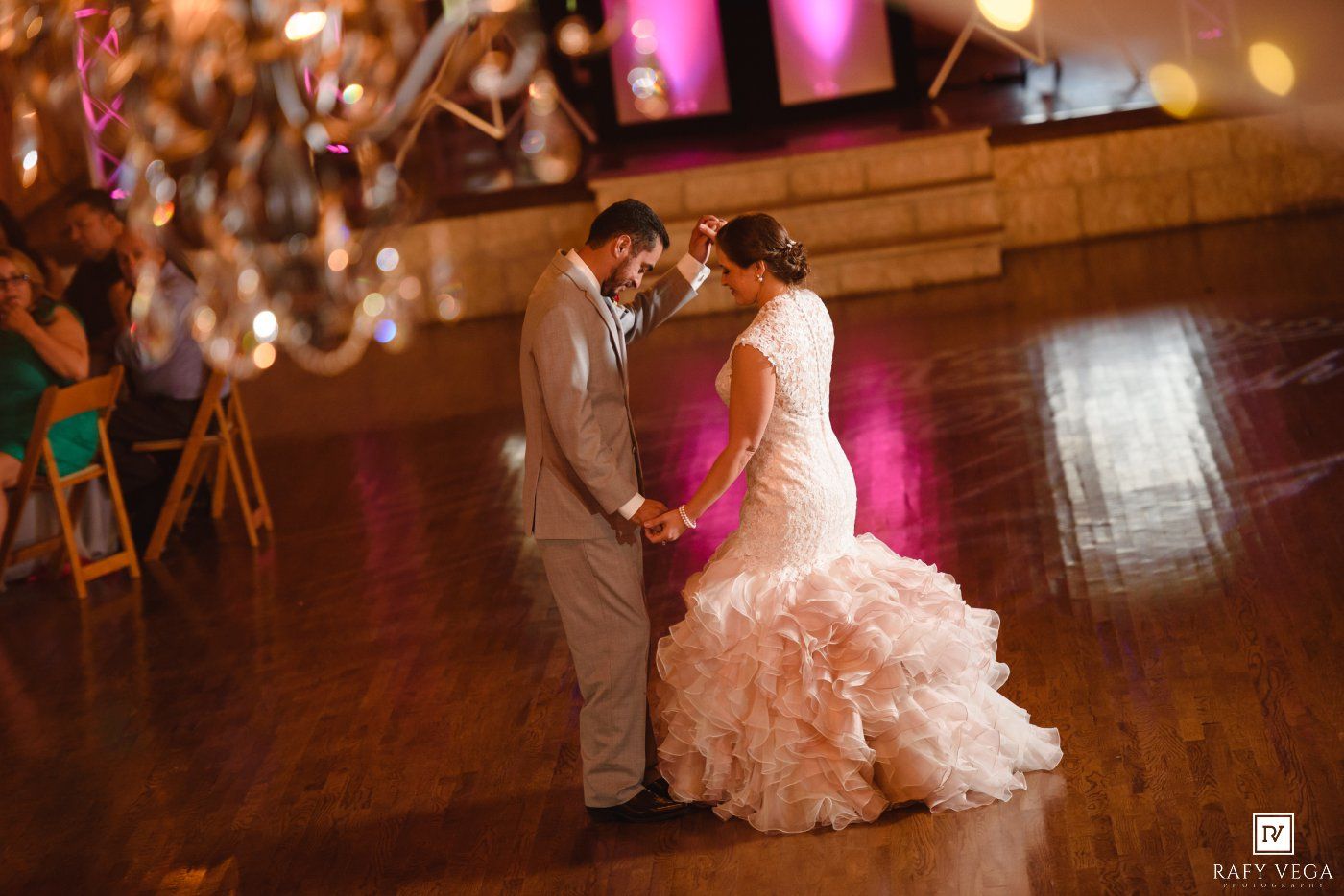 Bride and groom share their first dance on a glowing hardwood floor at an elegant wedding reception.