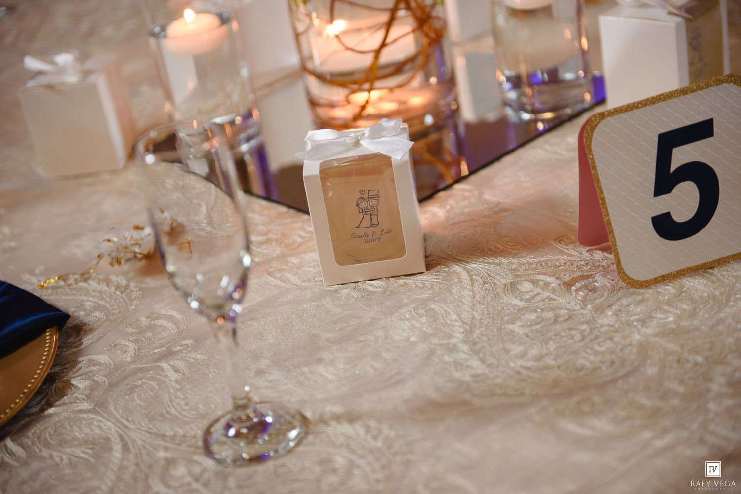 Elegant wedding reception table with ivory lace tablecloth, champagne flute, table number 5, and candlelit centerpiece.