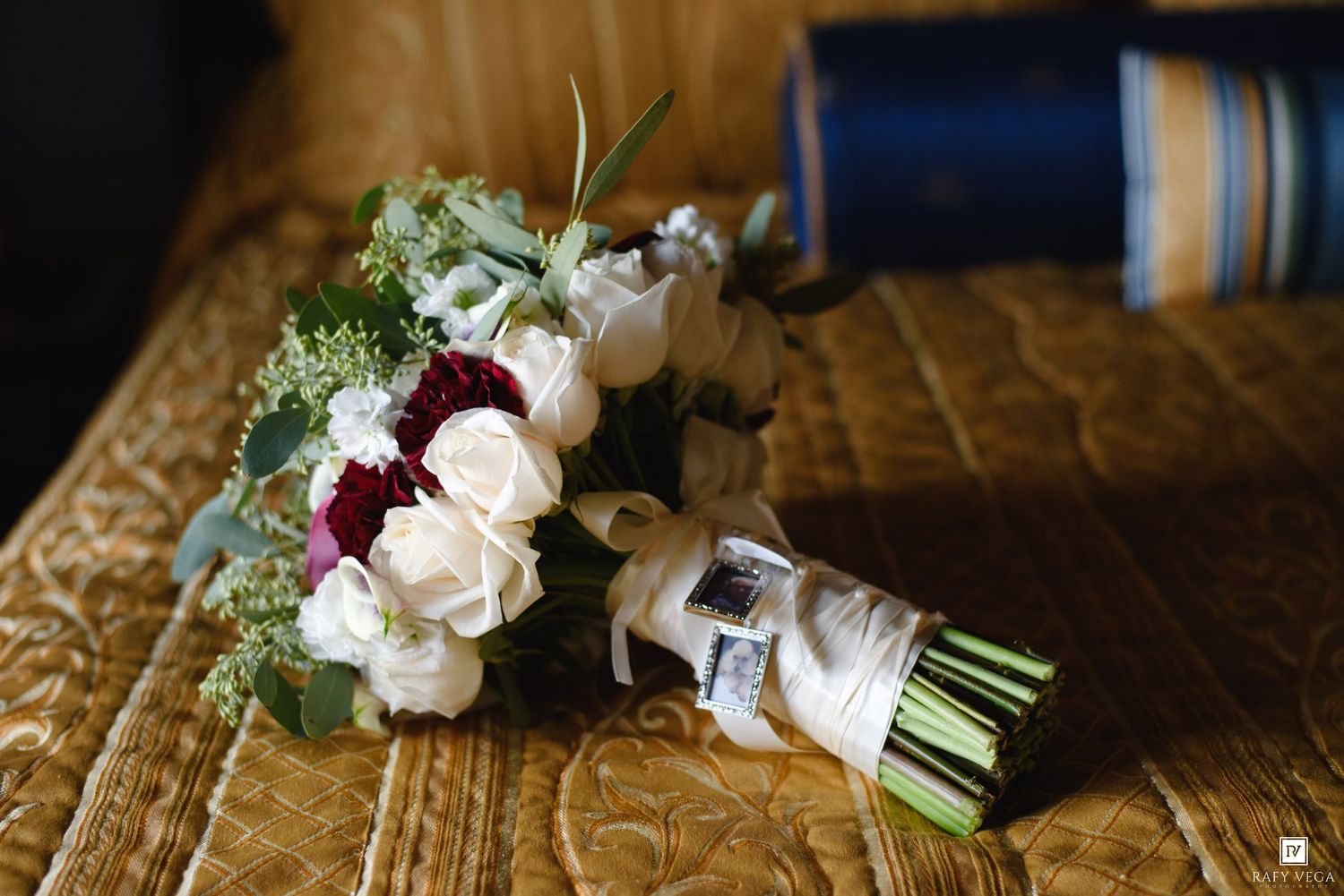Elegant wedding bouquet with white and burgundy roses and eucalyptus on a gold textured surface.