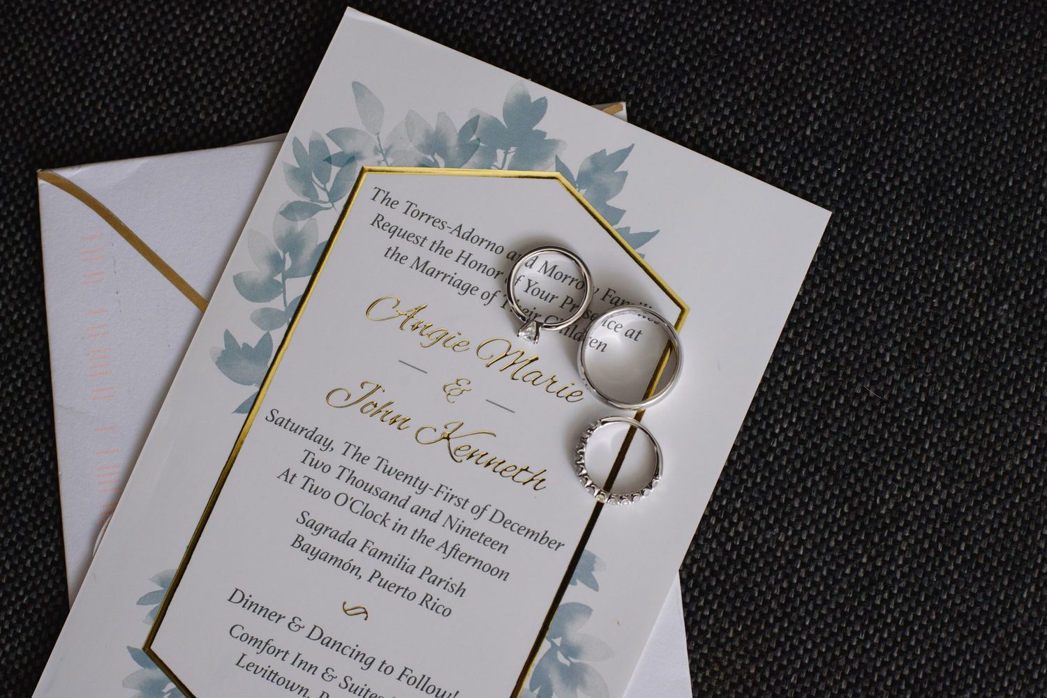 Wedding invitation with floral design displayed alongside two elegant rings on a white envelope.