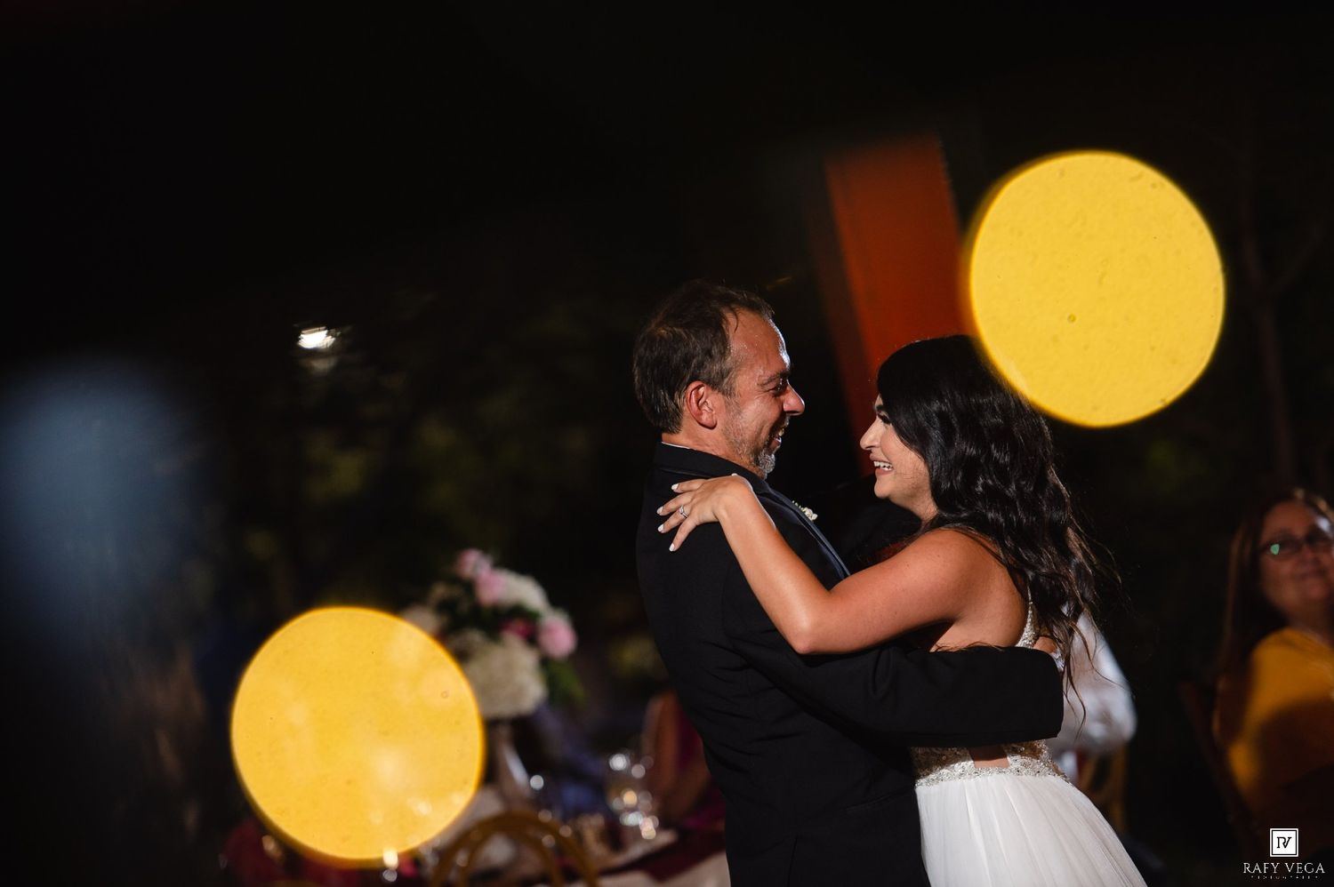 Couple sharing first dance at wedding reception with glowing moon lanterns in background at night.