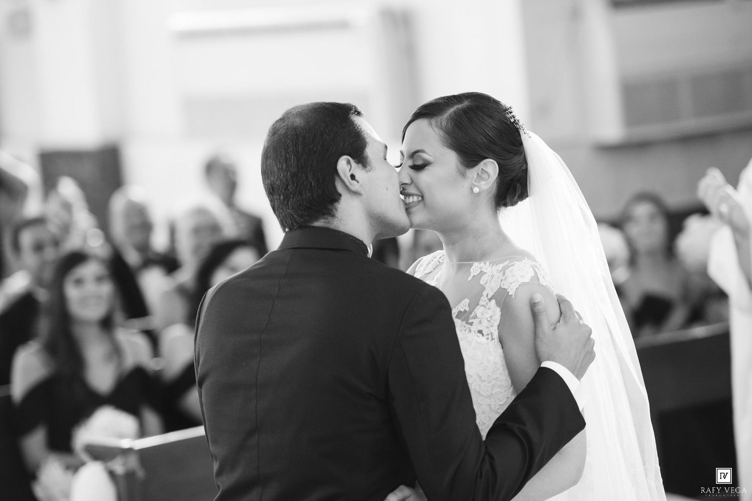 Bride and groom share first kiss at church wedding ceremony, surrounded by guests in pews.