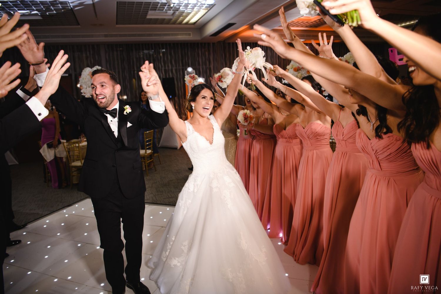 Bride and groom make grand entrance through tunnel of cheering bridesmaids in dusty rose gowns.