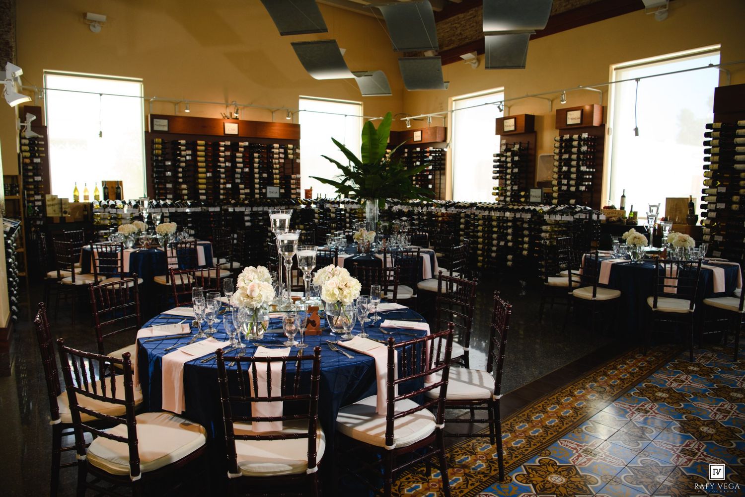 Elegant wedding reception in a wine cellar venue with navy blue tablecloths, floral centerpieces, and Chiavari chairs.