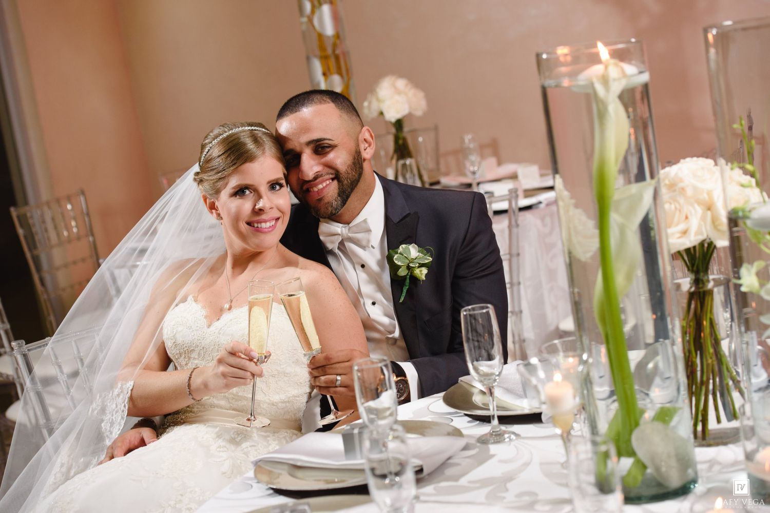 Bride and groom smiling together at wedding reception table with candles and white floral centerpieces.