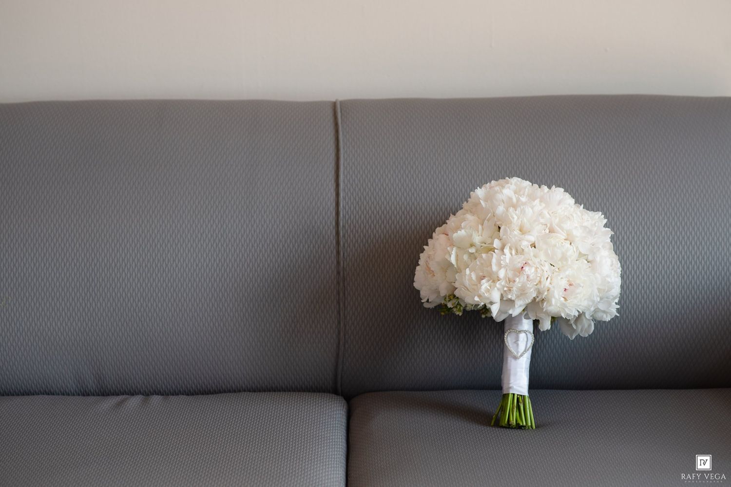 White hydrangea wedding bouquet with ribbon wrap resting on a modern gray leather sofa.