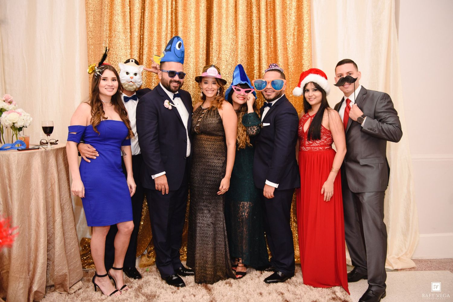 Group of eight elegantly dressed adults posing together at a formal party, wearing festive hats and accessories.
