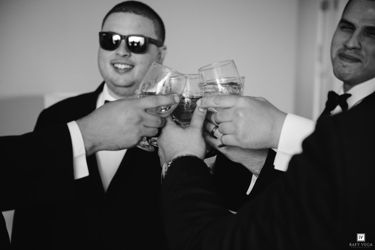 Groomsmen in suits toasting with glasses in a black and white wedding celebration photo.