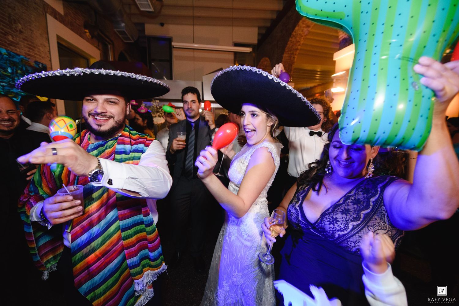 People in sombreros and colorful ponchos celebrate at a festive Mexican-themed wedding reception party.