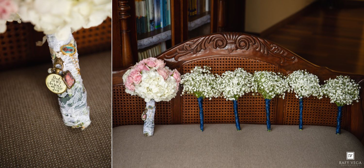 Wedding bouquets displayed on wooden chair, featuring pink roses, white hydrangeas, and baby's breath with navy blue ribbon handles.