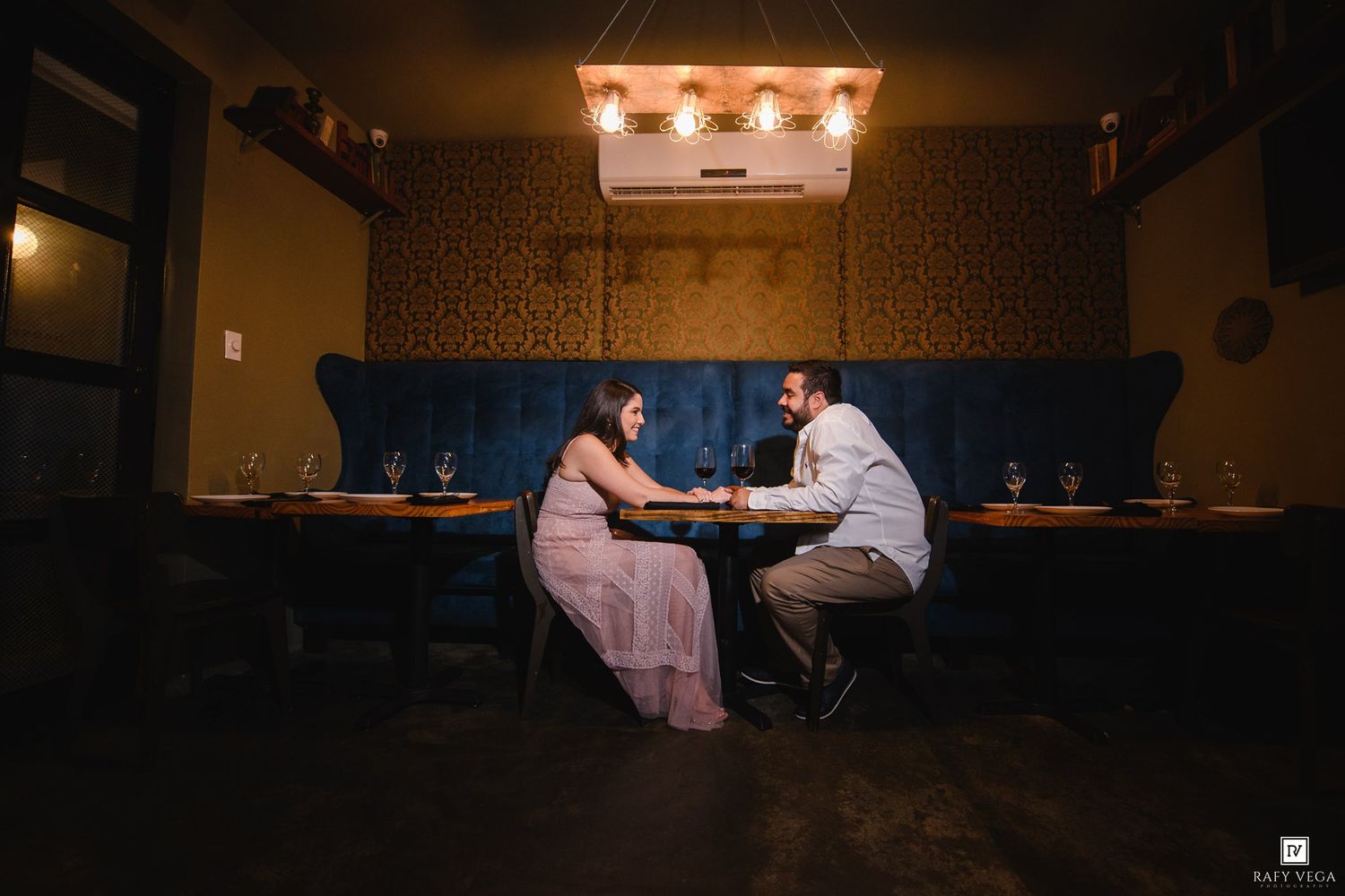 Couple sharing an intimate dinner at a dimly lit restaurant booth with warm pendant lighting and decorative wallpaper.