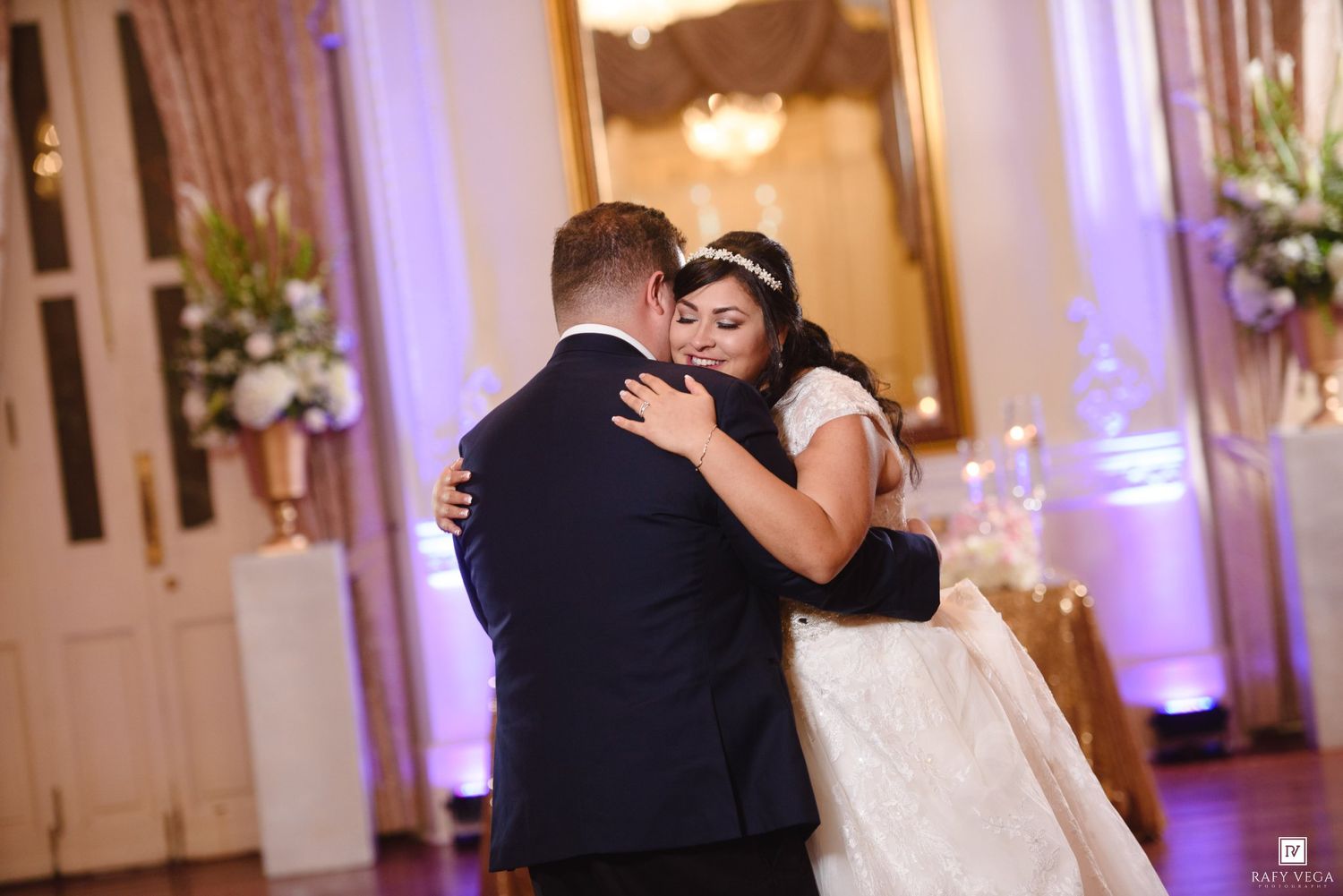 Couple shares romantic first dance embrace at luxurious wedding reception with floral arrangements.
