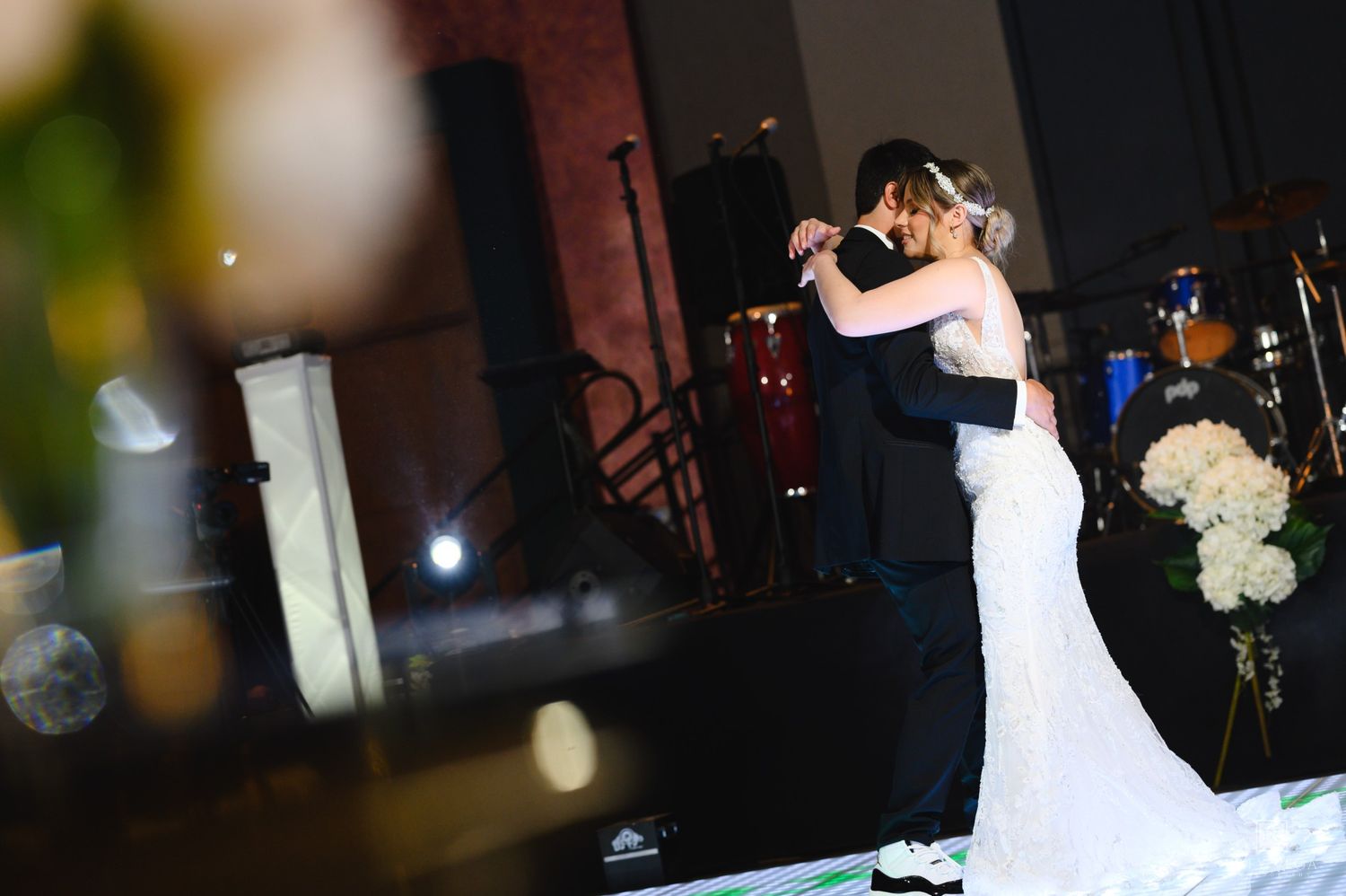 Bride and groom share their first dance, embracing closely on a softly lit wedding reception dance floor.