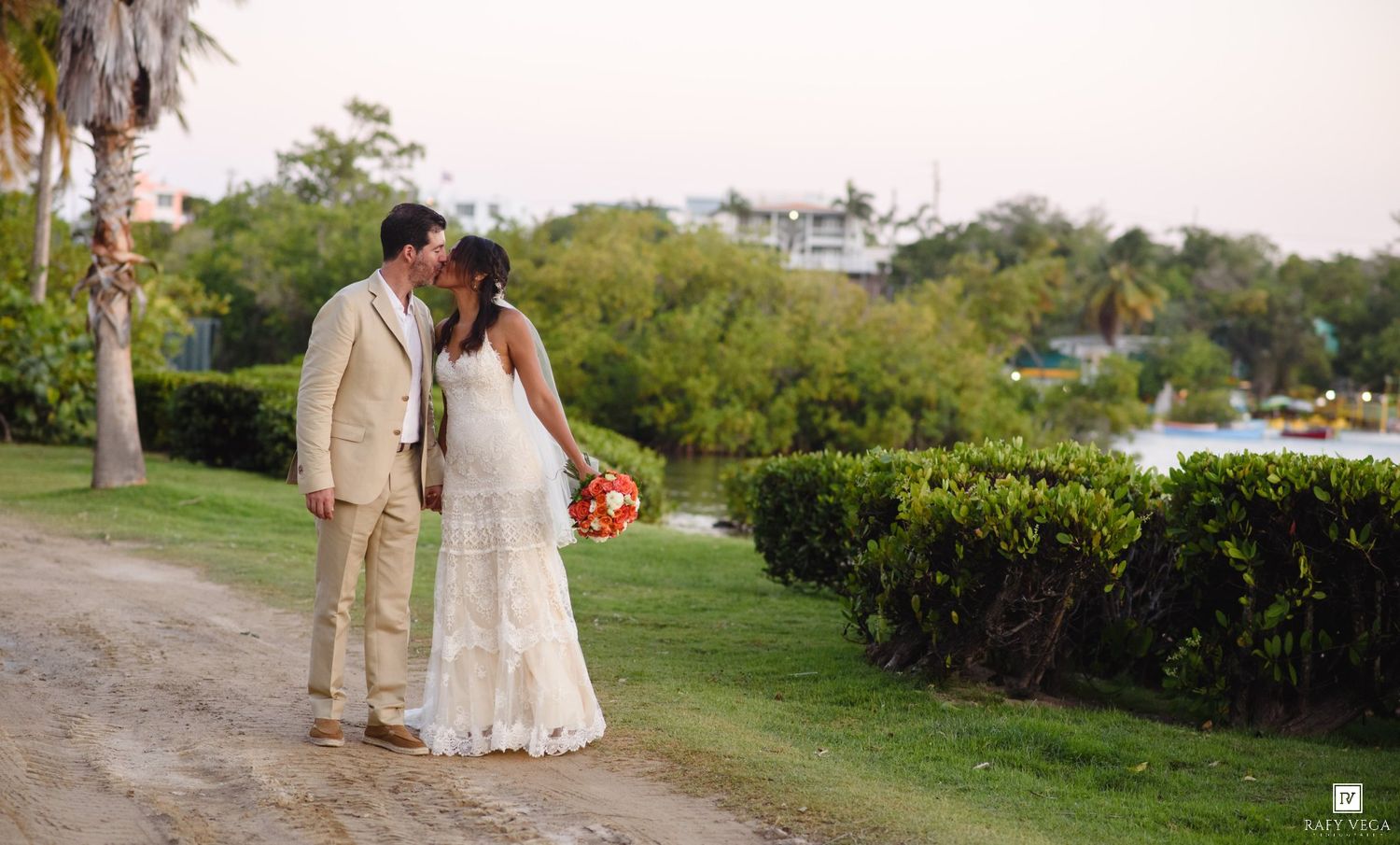 A bride and groom share a romantic kiss on a scenic garden path at their outdoor wedding ceremony.