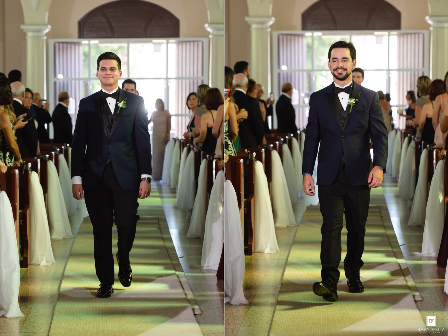 Two groomsmen in black tuxedos walking down a wedding aisle lined with white floral arrangements.