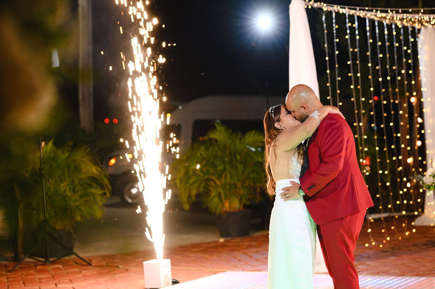 Couple sharing romantic kiss during first dance with sparkling fountain fireworks at night.