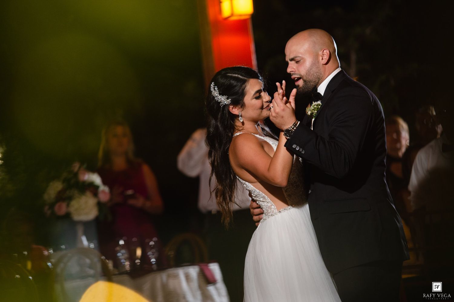 Bride and groom share their first dance at an outdoor wedding reception under warm evening lights.