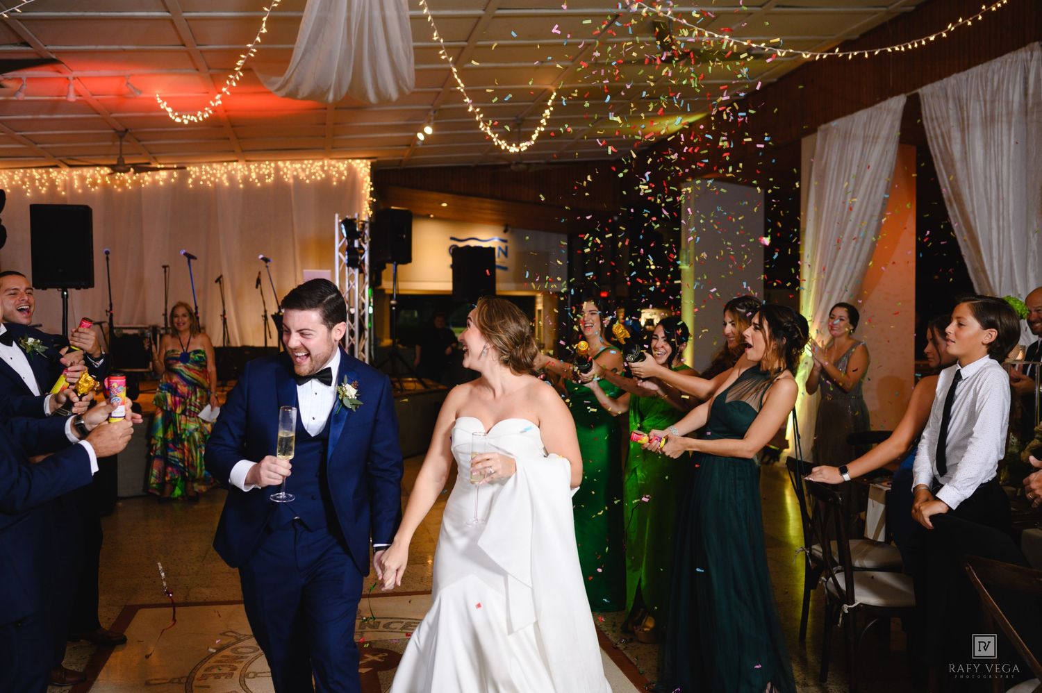 Bride and groom celebrate at wedding reception with confetti and cheering guests in elegant venue.