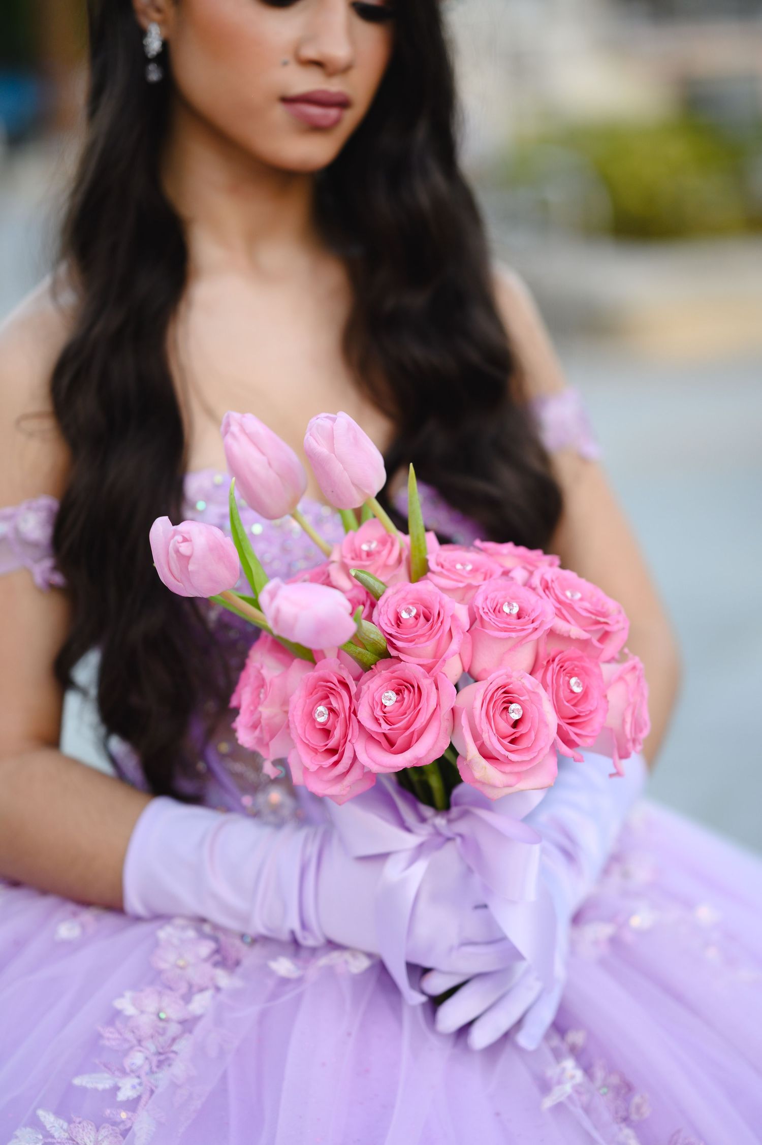 Young woman in lavender ball gown and gloves holding pink roses and tulip bouquet for quinceañera celebration.