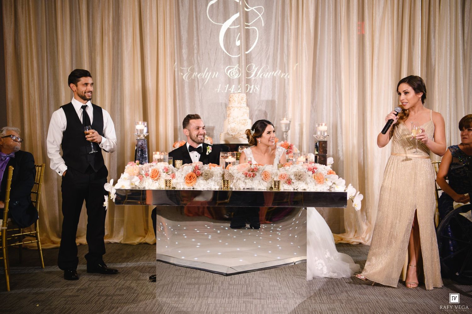 Best man and maid of honor giving wedding speeches at elegant reception with floral centerpiece sweetheart table.