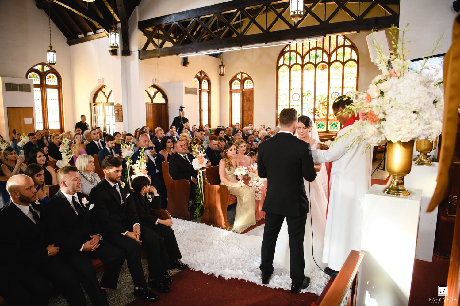 A wedding ceremony in a church with guests seated in pews as the groom stands at the altar with the bride.