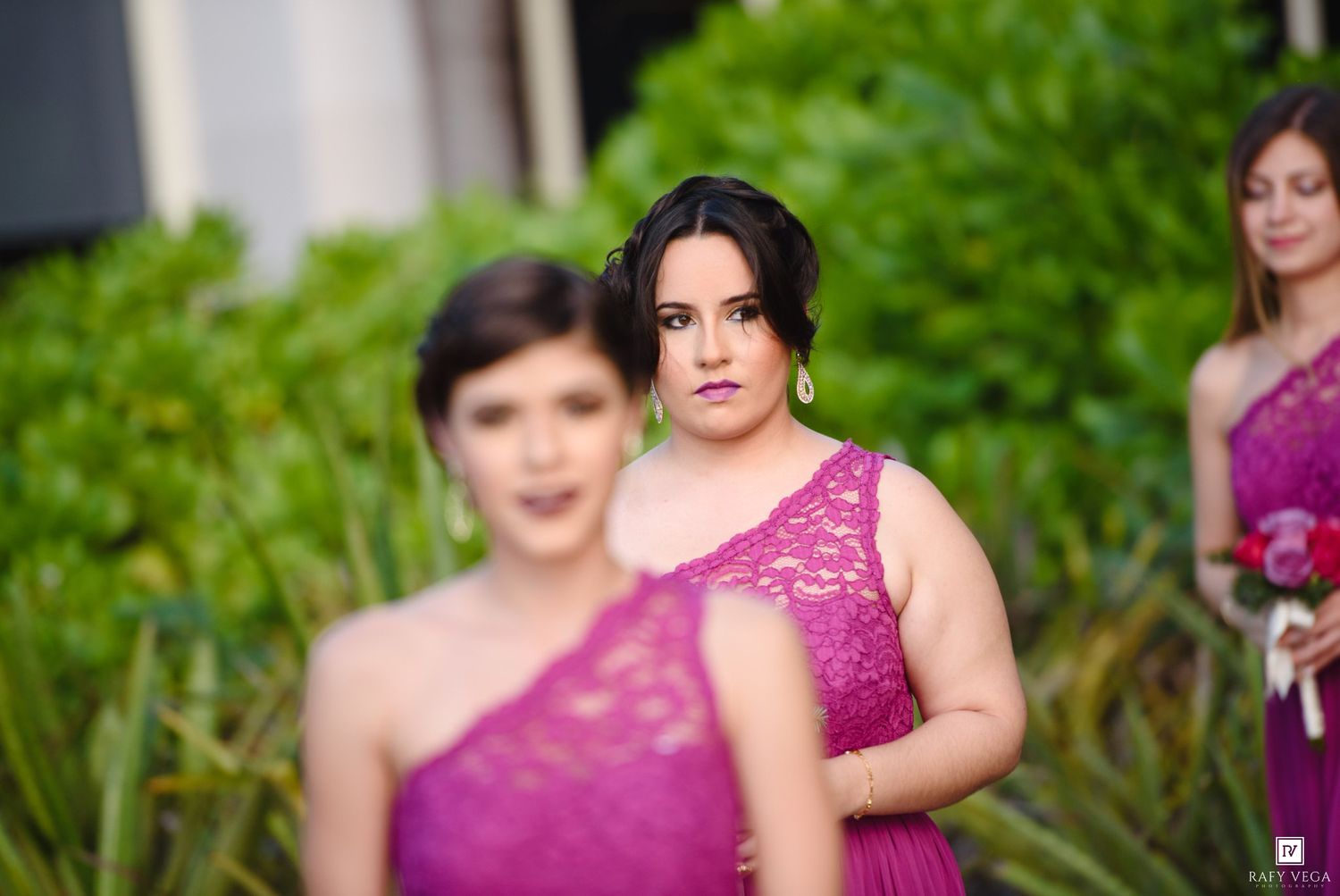 Bridesmaids in purple dresses pose outdoors with green foliage background at a wedding ceremony.