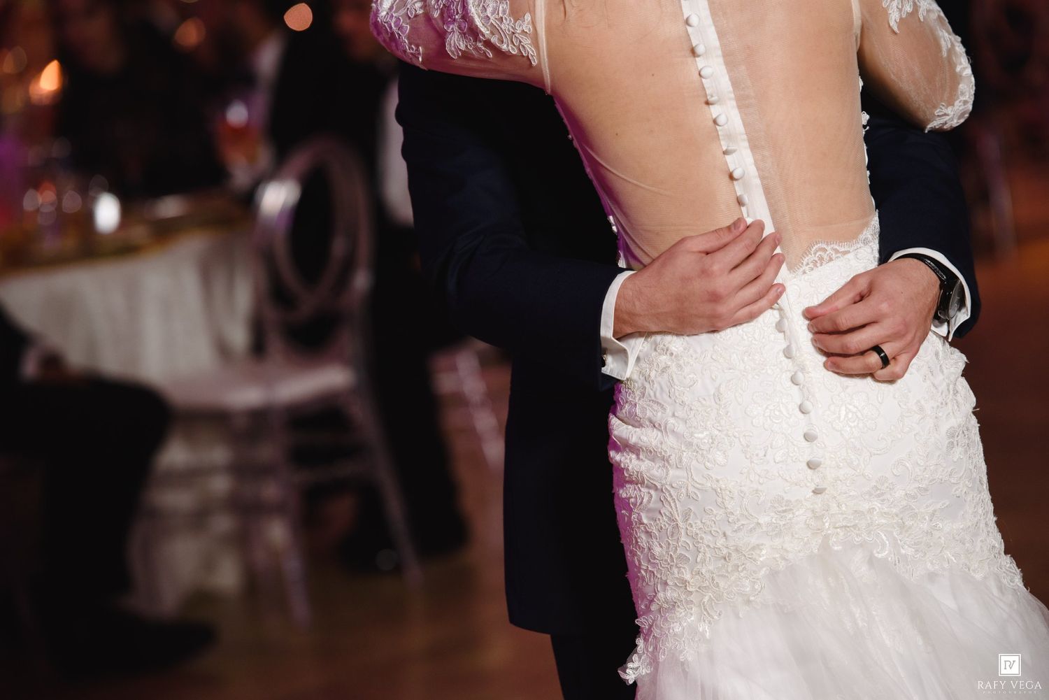 Bride and groom sharing first dance, showcasing elegant lace button-back wedding gown at reception.