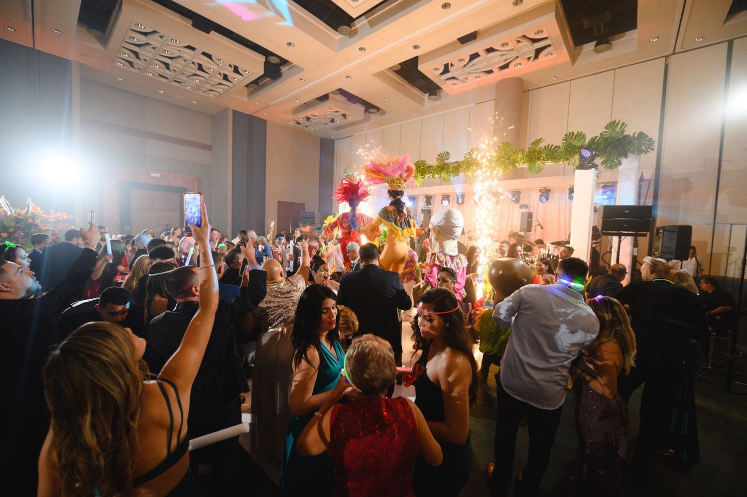 Lively wedding reception with guests dancing as a colorful performer parade enters the ballroom with sparklers.