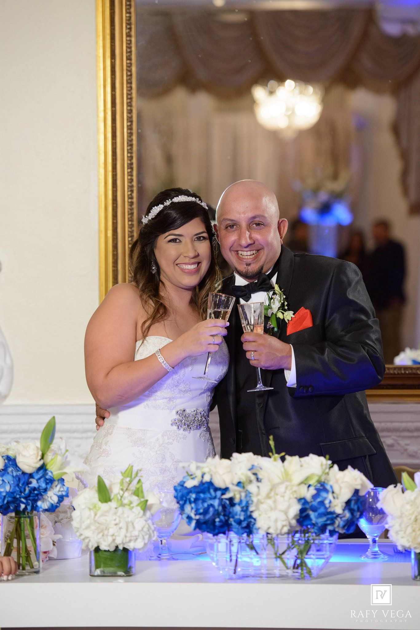 Bride and groom toasting with champagne at wedding reception, surrounded by blue and white floral centerpieces.