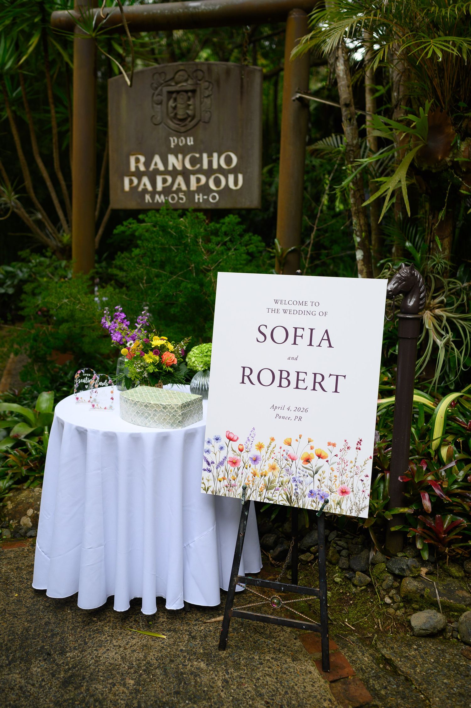 Wedding welcome sign for Sofia and Robert on an easel at Rancho Papapou venue, surrounded by lush greenery and floral arrangements.