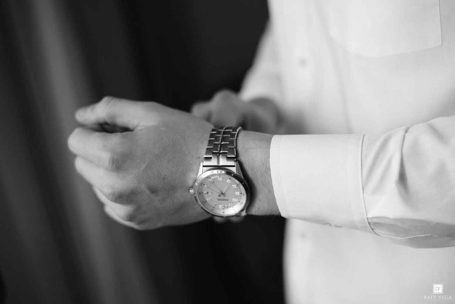 Black and white photo of a groom adjusting his silver wristwatch while wearing a white dress shirt.