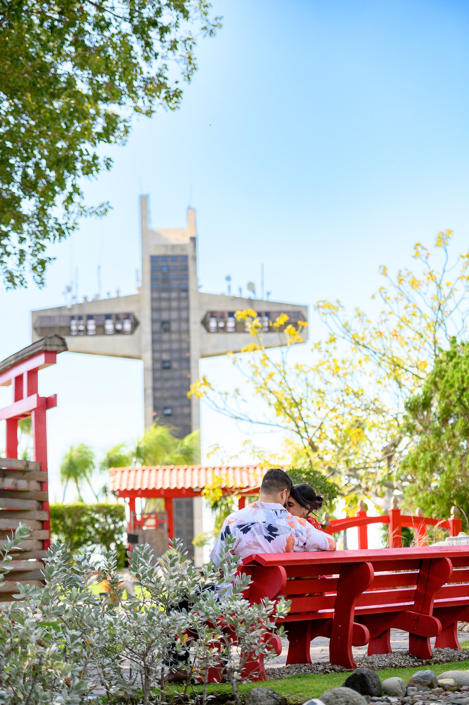 Couple sitting on a red bench in a Japanese garden with a modern building in the background.