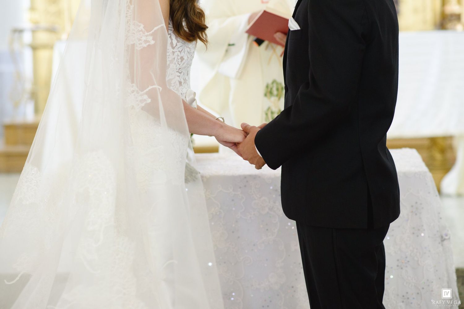 Bride and groom holding hands at church altar during wedding ceremony, bride in white gown with veil.