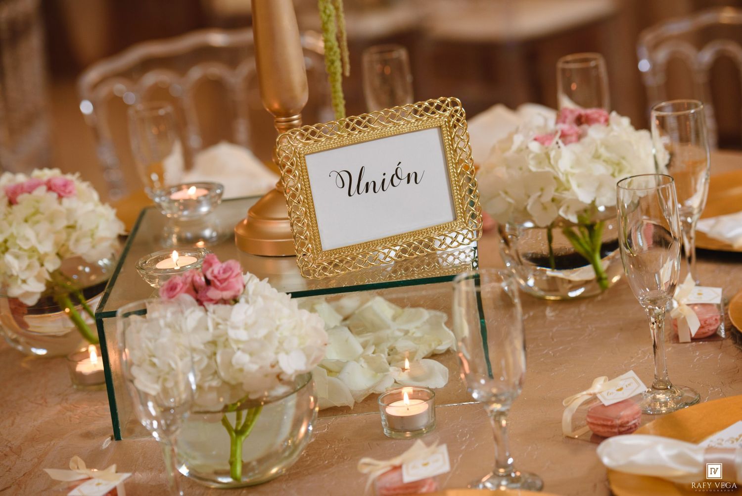 Elegant wedding reception table with white and pink floral centerpieces, candles, and a gold-framed Union table number sign.
