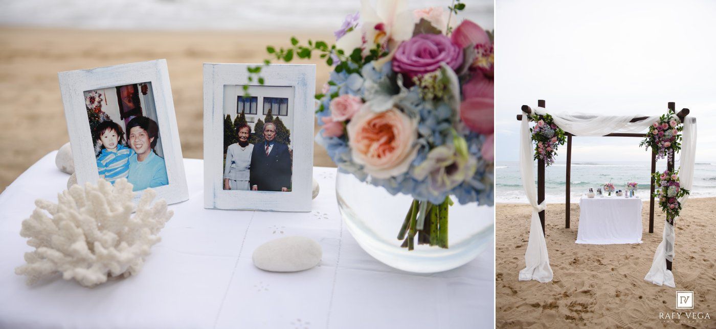 Beach wedding decor with framed photos, coral, floral bouquet, and a decorated arch on sandy shore.