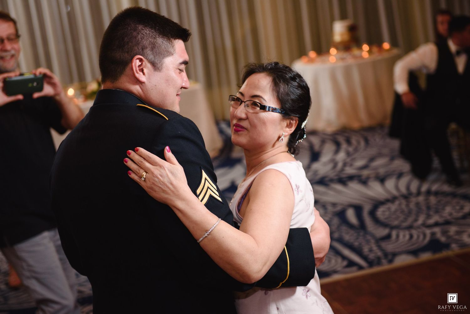 Military groom and mother share an emotional first dance at elegant wedding reception ballroom.