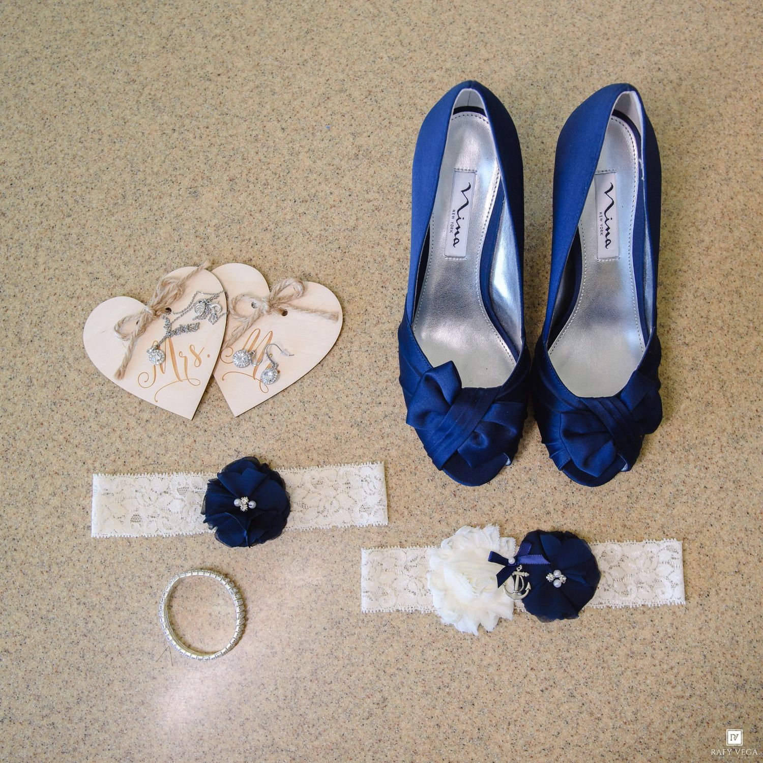 Blue peep-toe wedding heels with bow detail, lace garter set, and heart-shaped gift tags arranged on a neutral background.