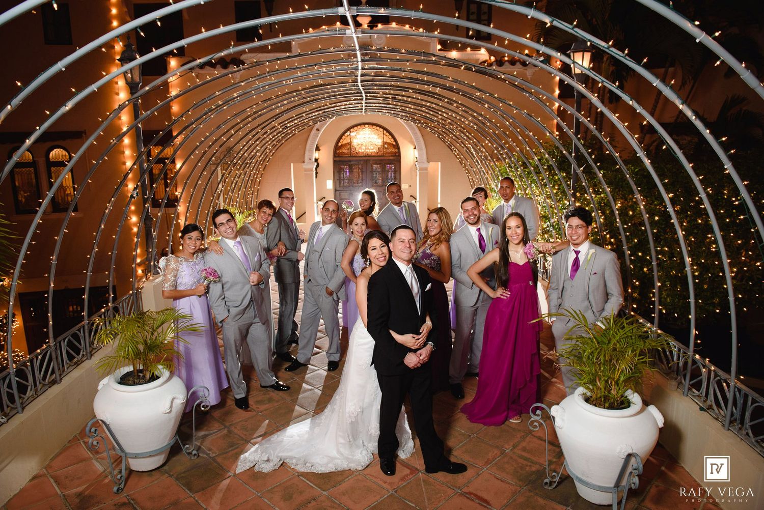 Wedding party poses under a sparkling light arch tunnel at an elegant outdoor venue.